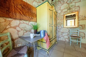 A stone-walled room with a yellow cabinet, a table with a kettle, a chair, and a framed mirror. - Room 'Masseria Copertini - Angelo' with Wi-Fi and Air Conditioning (Vernole)