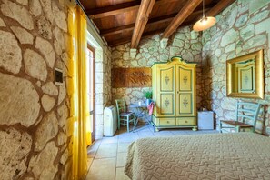 A stone-walled room with a bed, a yellow cabinet, a small table with a plant, and a chair. - Room 'Masseria Copertini - Angelo' with Wi-Fi and Air Conditioning (Vernole)