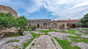 Un patio con un camino de piedra, césped verde y un edificio con ventanas de arco y tejado de tejas.