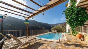 A stone pool with lounge chairs, a pergola with hanging lights, and a mountain view.