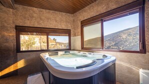 A bathroom with a hot tub, a window with a view of a hilly landscape, and a wooden ceiling.
