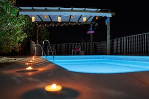 Une piscine avec une terrasse en bois, un espace salon couvert et une rambarde.