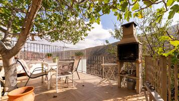 Une terrasse extérieure avec une table et des chaises, un barbecue et une vue sur un paysage montagneux.