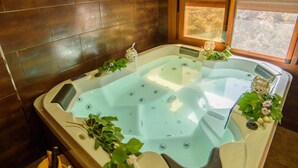 Ein Whirlpool mit Holzwand und Fenster, umgeben von viel Grün und einer Weinflasche.