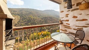 Ein Balkon mit Blick auf eine gebirgige Landschaft, inklusive Tisch, Stühlen und einer hängenden Blumenampel.