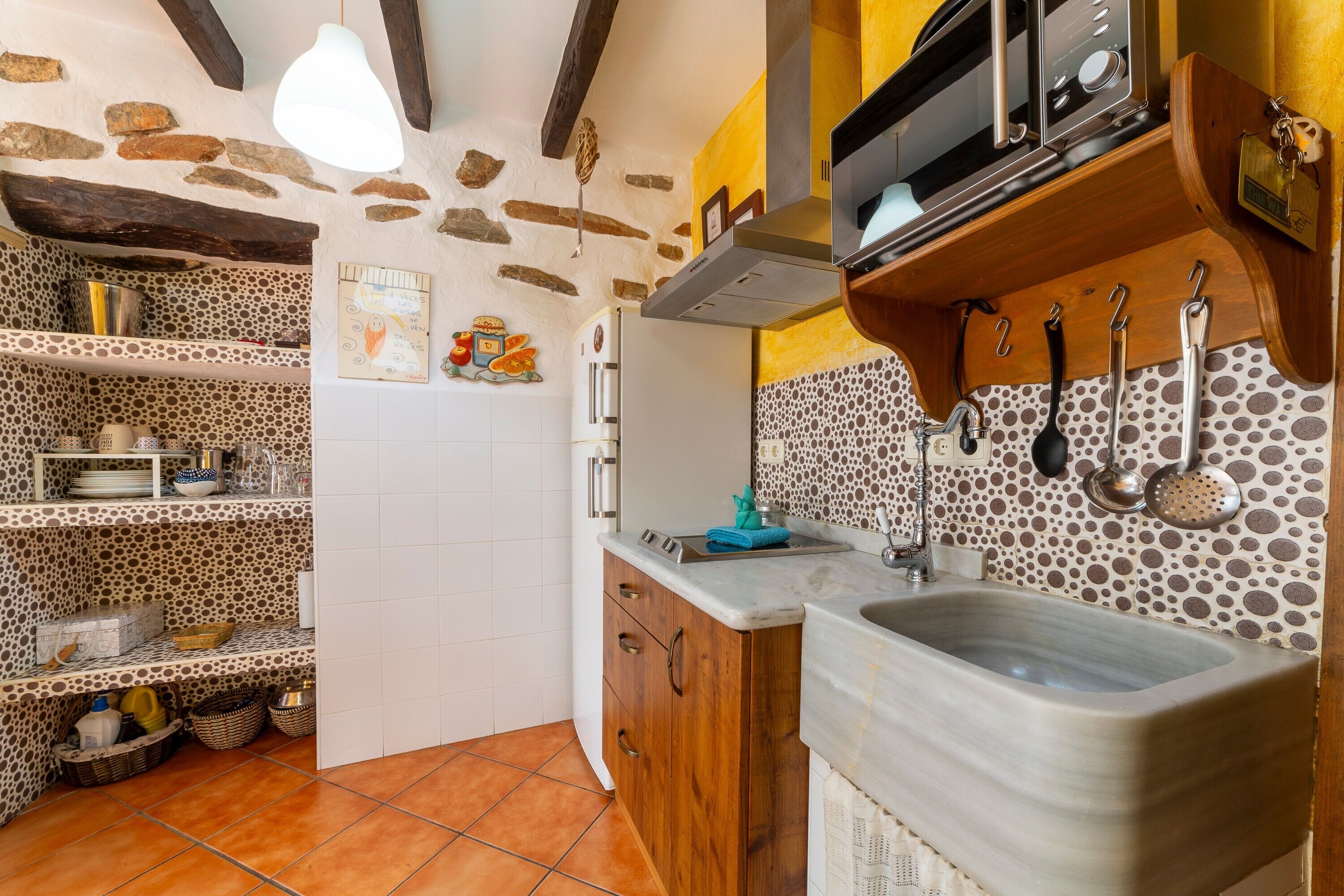 A kitchen with stone walls, wooden cabinets, a sink, and a stove.