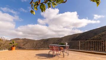 Una terraza con mesa y sillas, una planta en maceta y vistas a un paisaje montañoso.