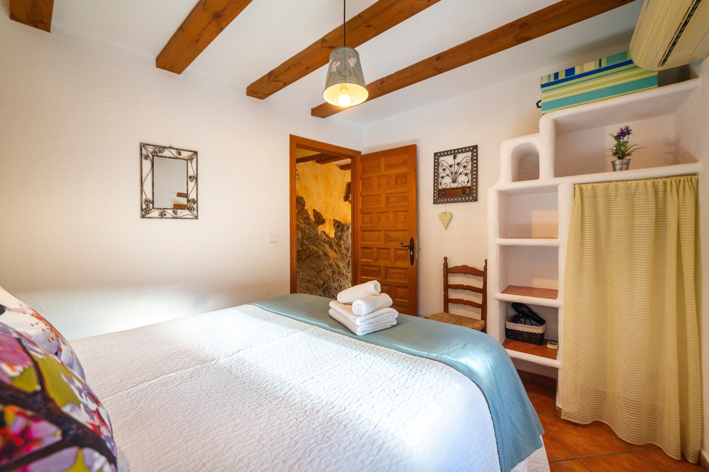 A bedroom with a bed, a wooden door, a shelf with a plant, and a hanging light fixture.