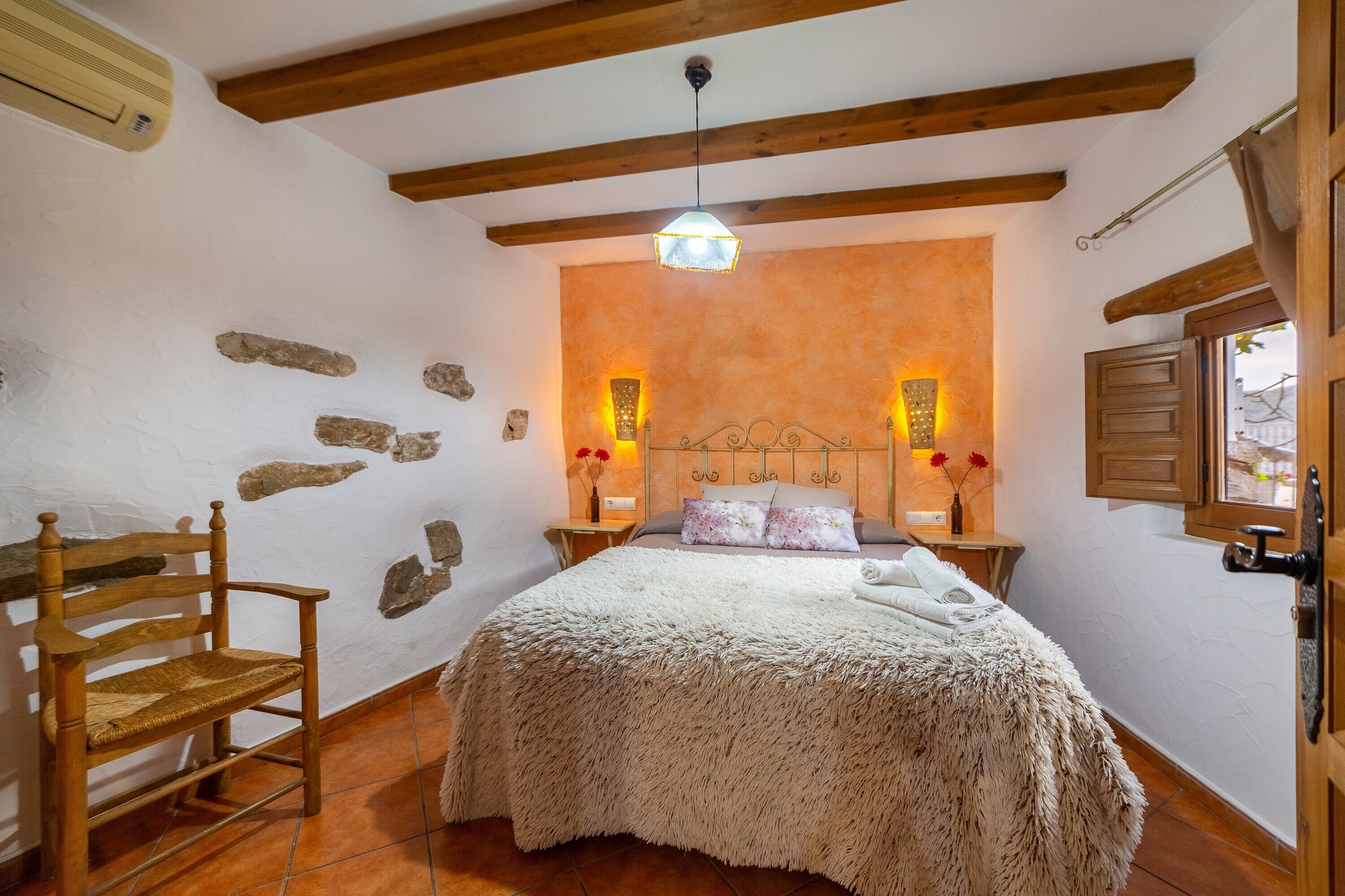A bedroom with a wooden bed, a rocking chair, stone wall decorations, and a stone fireplace.