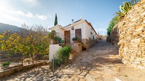 A stone-paved street leading to a white building with a balcony and potted plants. - Country House 'C´antonia Y Manuel' with Mountain View, Wi-Fi and Air Conditioning (Laroya)