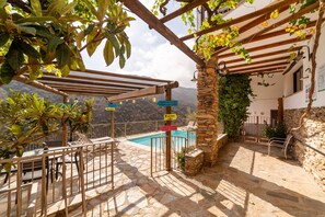 A stone patio with a pool, outdoor seating, and a pergola.