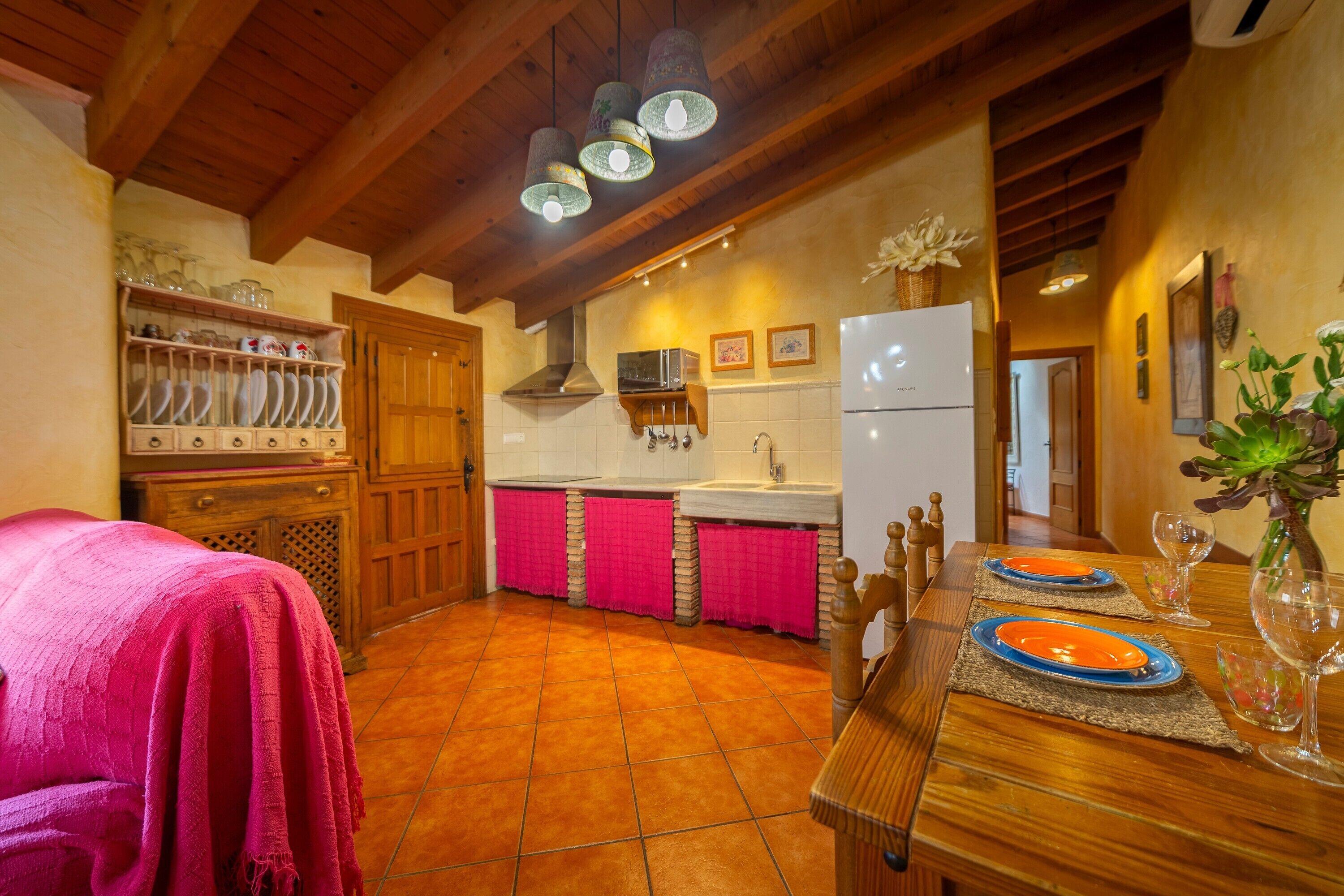 Una cocina con armarios de madera, un lavamanos y una mesa de comedor con platos y vasos.