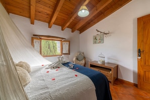 A bedroom with a bed, wooden ceiling beams, a window, a chair, a bedside table, and a door. - Country House 'Tenguerengue' with Mountain View, Wi-Fi and Air Conditioning (Laroya)