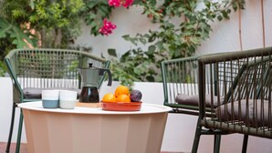A table with a coffee maker, two cups, and a bowl of fruit.