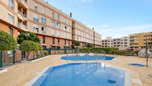 A swimming pool area with two pools, surrounded by a brick building with balconies, and a clear sky.