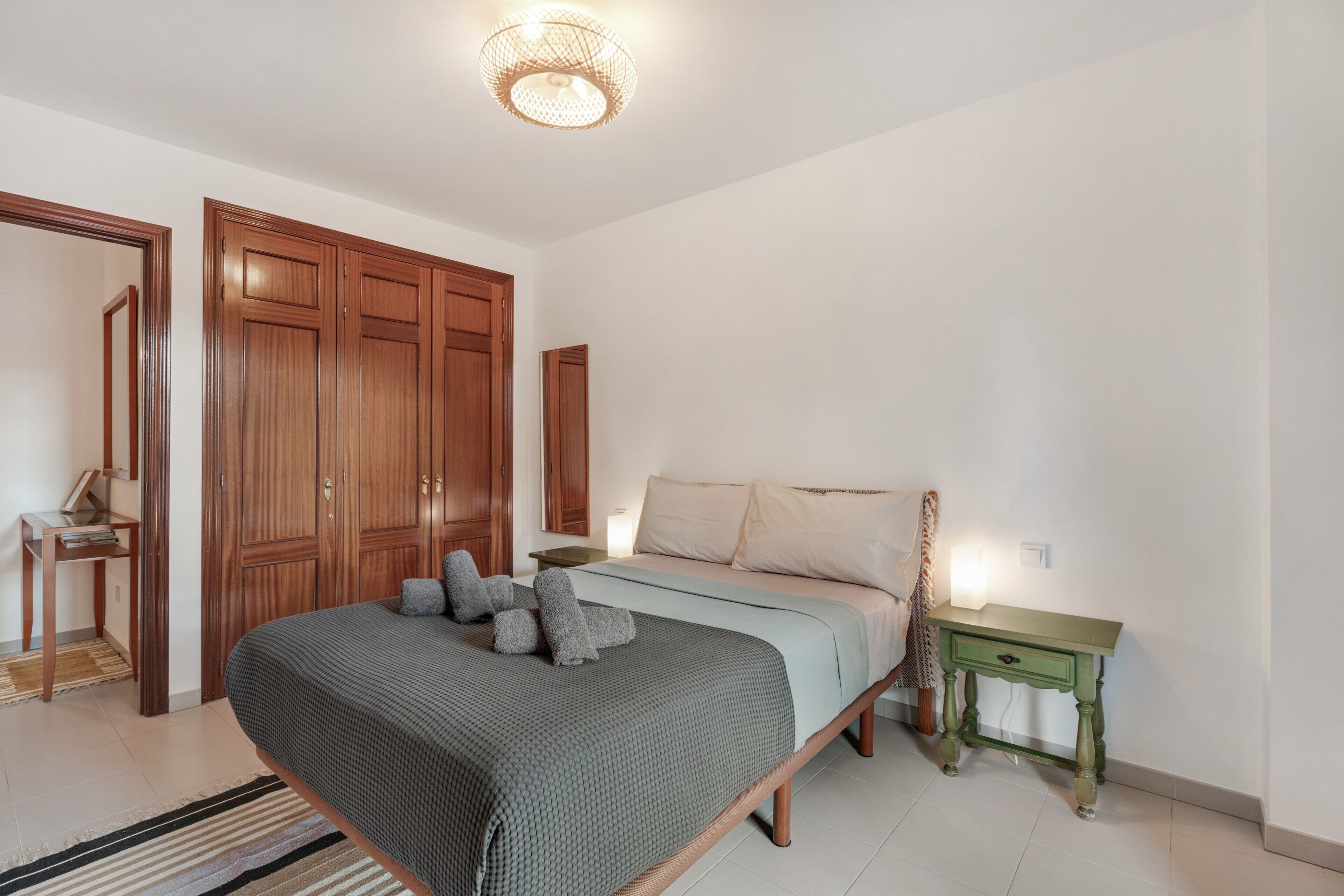 Un dormitorio con cama, armario de madera, mesita de noche y lámpara colgante.
