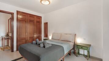 Un dormitorio con cama, armario de madera, mesita de noche y lámpara colgante.