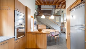 Une cuisine dotée de meubles en bois, d’un four encastré, d’un réfrigérateur, de luminaires suspendus et d’un coin repas avec une table et des chaises.