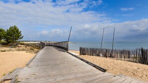 A wooden boardwalk leading to a beach with a fence on one side and a clear sky above.