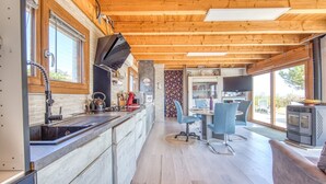 A modern kitchen with wooden beams, a large window, and a dining area with a TV.