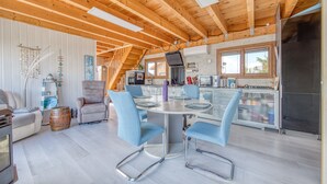 A modern kitchen with a central island, a dining area with blue chairs, and a wooden ceiling.