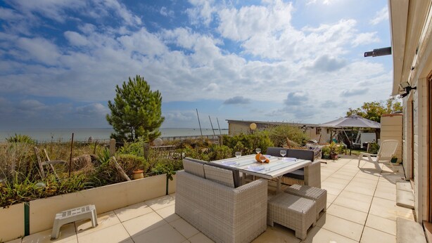 An outdoor patio with a table and chairs, a view of the sea, and a wooden fence.