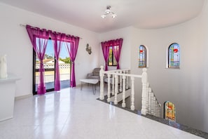 Une pièce spacieuse avec un escalier blanc, une petite table et des rideaux violets.