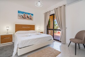 A bedroom with a bed, bedside tables, a chair, a painting, and a view through a glass door. - Holiday Home 'Villa Das Nogueiras' with Sea View, Wi-Fi & Air Conditioning (Lagoa)