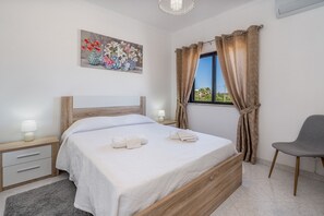 A bedroom with a bed, bedside tables, a chair, a window with curtains, and a painting on the wall.