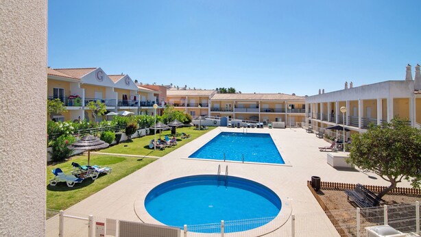 A hotel with a swimming pool, sun loungers, and a garden area.