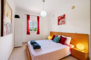 A bedroom with a bed, bedside lamps, a window with curtains, a door, and a wall with a painting. - Encosta São José Apartment with Shared Pool, Wi-Fi, and Air Conditioning (Guia)
