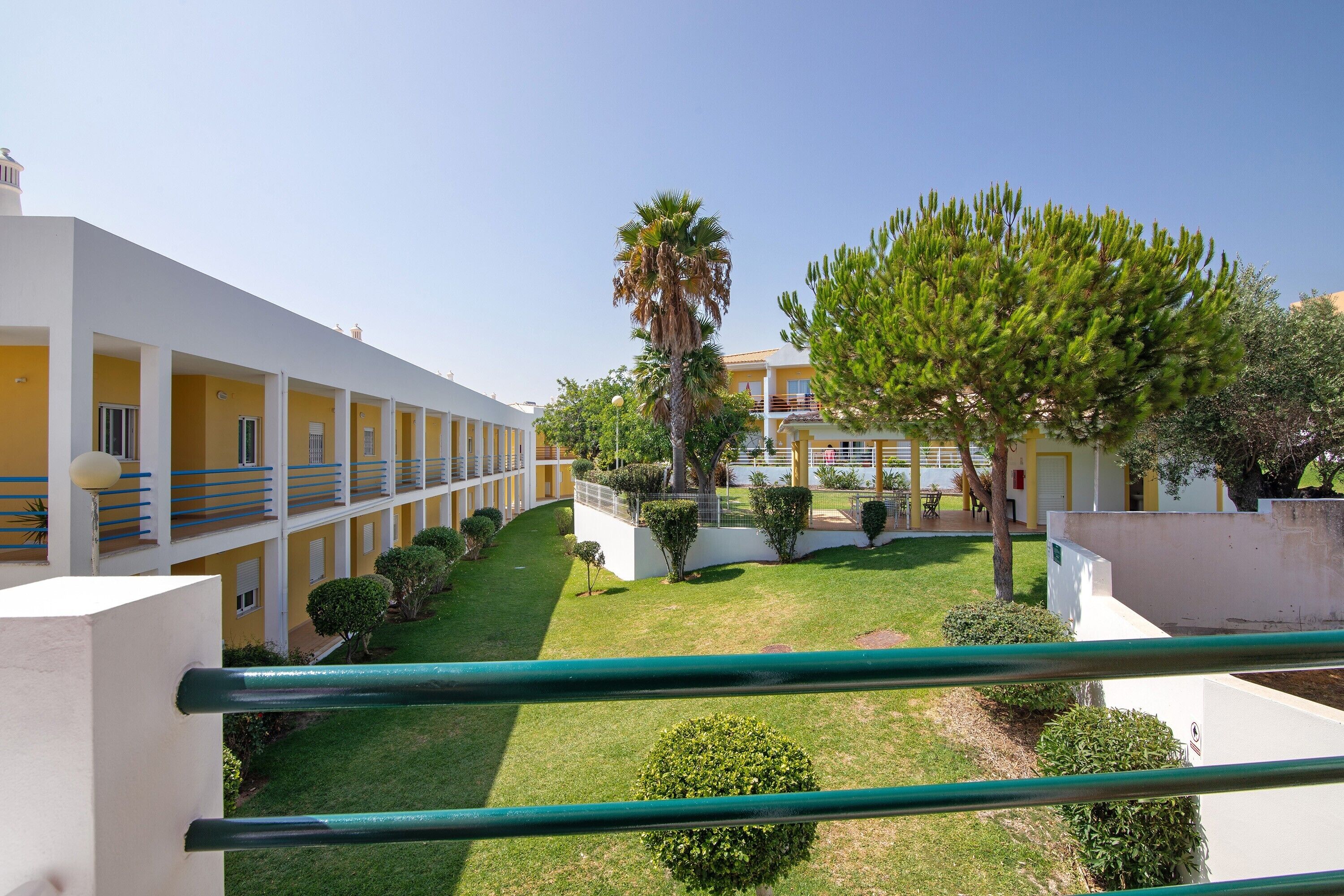 Un patio de hotel con un césped central, rodeado de edificios con balcones y una palmera.