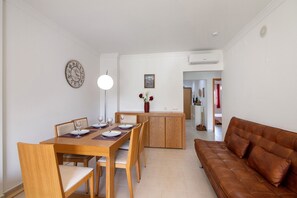A dining area with a wooden table, chairs, and a brown leather sofa. - Encosta São José Apartment with Shared Pool, Wi-Fi, and Air Conditioning (Guia)