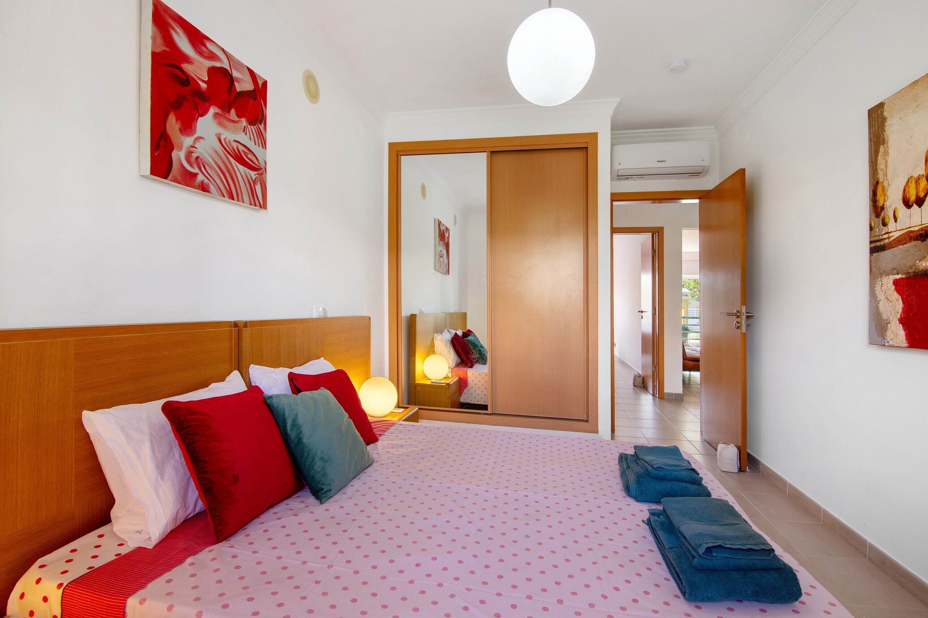 Une chambre d’hôtel avec un lit, des oreillers, une lampe de chevet, une armoire et un miroir.