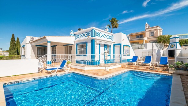 Une piscine à l’eau bleue, des bâtiments blancs et bleus, et des chaises longues.