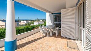 Un balcon avec une table et des chaises, une vue sur la mer et un bâtiment avec des volets.
