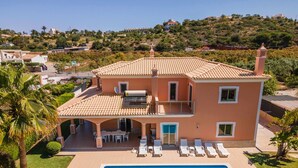 Una casa de dos pisos con piscina, un porche cubierto y vistas a un paisaje montañoso.