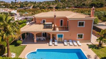 Una casa de dos pisos con piscina, un porche cubierto y vistas a un paisaje montañoso.