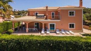 Una casa de dos pisos con techo de tejas, un balcón y una piscina con sillas de descanso.