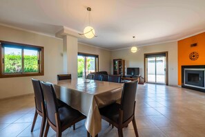 A spacious dining area with a large table and chairs, a kitchen in the background, and a fireplace. - Villa 'Hunês' with Private Pool, Wi-Fi and Air Conditioning (Guia)