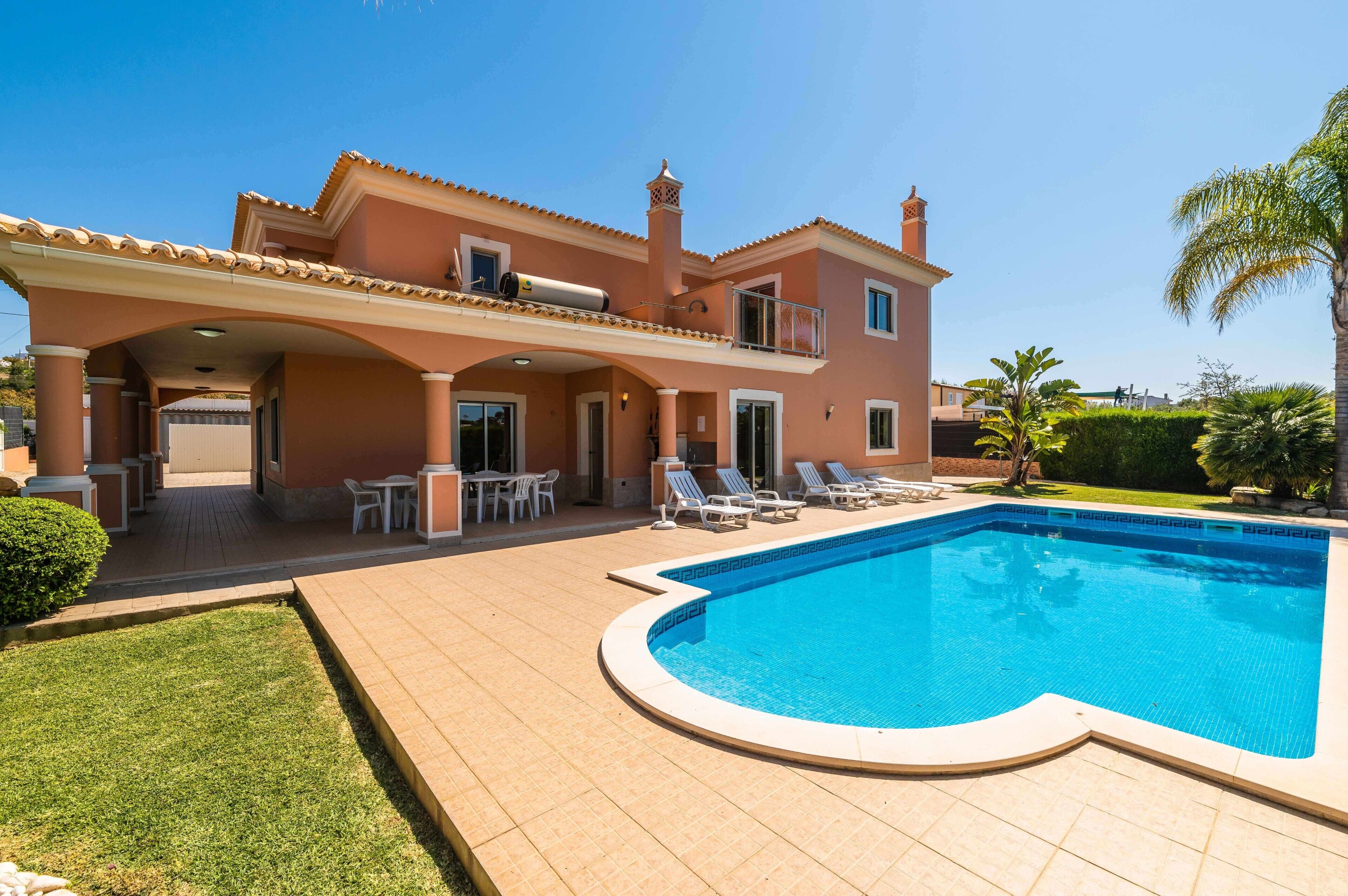 Una casa de dos pisos con piscina, mobiliario exterior y terraza cubierta.