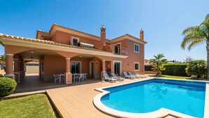 Una casa de dos pisos con piscina, mobiliario exterior y terraza cubierta.