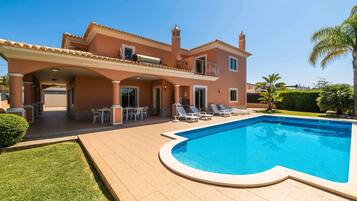 Una casa de dos pisos con piscina, mobiliario exterior y terraza cubierta.