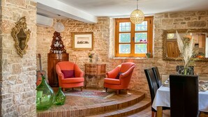 A cozy room with stone walls, a wooden cabinet, two orange armchairs, a dining table with chairs, and a large window with a view. - Vacation home Bepo by Interhome (Poreč/Heraki)