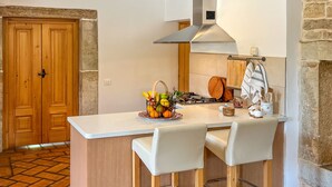 A kitchen with a central island, two bar stools, a stove, and a hanging rack with kitchen utensils. - Vacation home Bepo by Interhome (Poreč/Heraki)