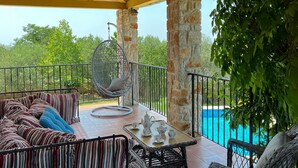 A covered outdoor seating area with a pool, striped sofa, hanging chair, and wicker chairs. - Vacation home Bepo by Interhome (Poreč/Heraki)