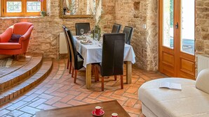 A dining area with a stone wall, a wooden table set for four, and a red armchair. - Vacation home Bepo by Interhome (Poreč/Heraki)