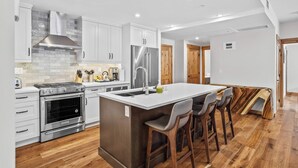 A modern kitchen with a central island, stainless steel appliances, and wooden flooring. - 114 Two Bedroom Premier Condo (Canmore)
