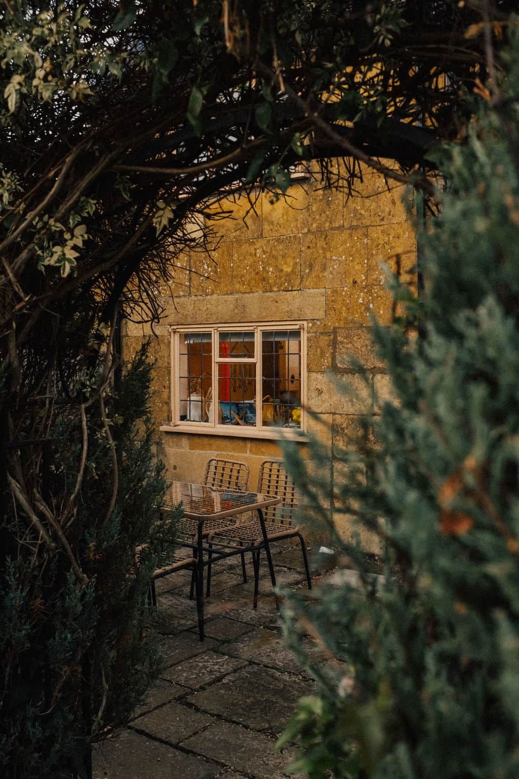 A rustic stone building with a window and a table with chairs outside.