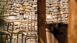 A rustic outdoor dining area with a stone wall backdrop, wicker table, and metal chairs. - Broadway Scandi Chic Cottage (Broadway)